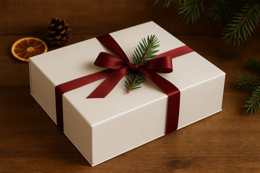 Eine weiße Geschenkbox mit roter Schleife und Tannenzweig als Deko